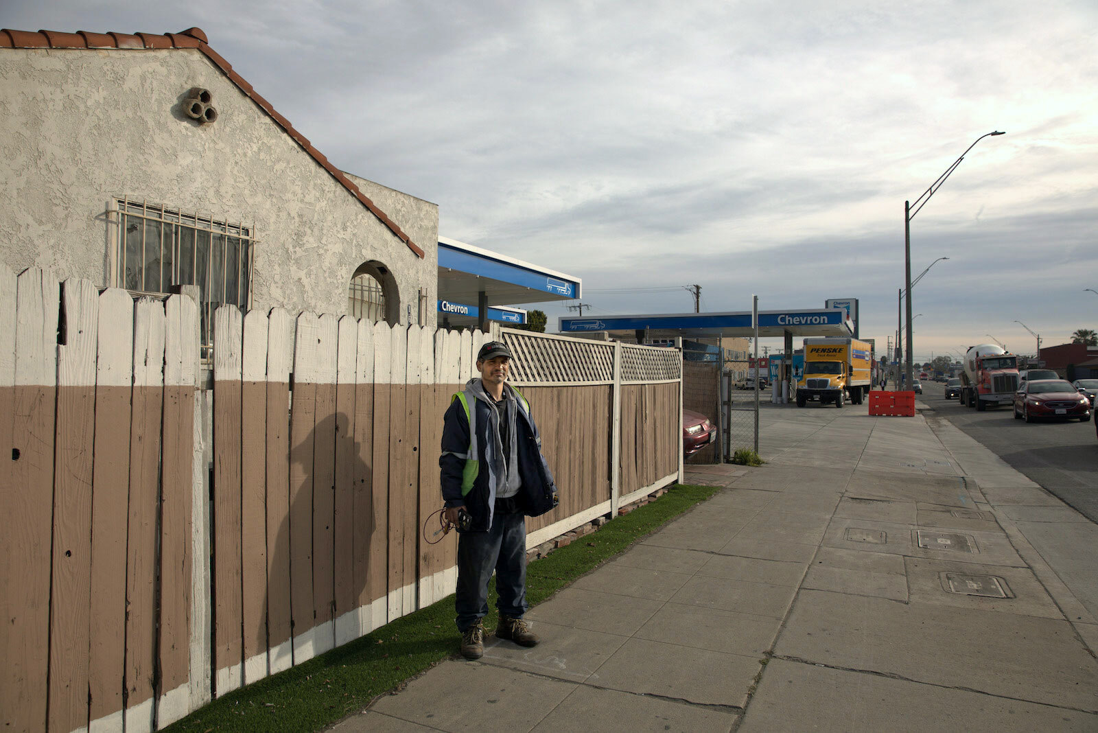 a man stands in front of a fence that divides a house from a gas station