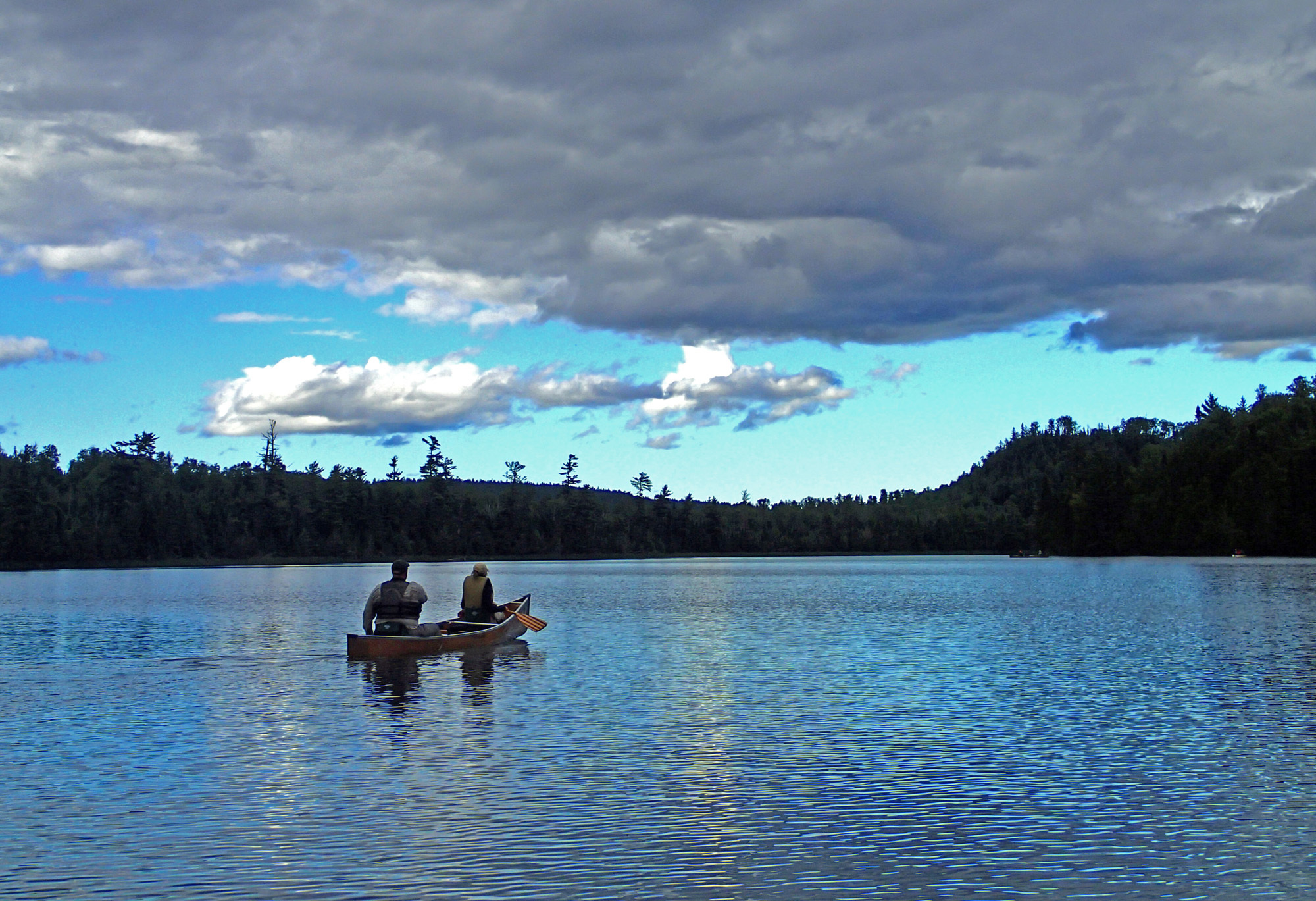 two people in a canoe paddle on a lake with forest in the background