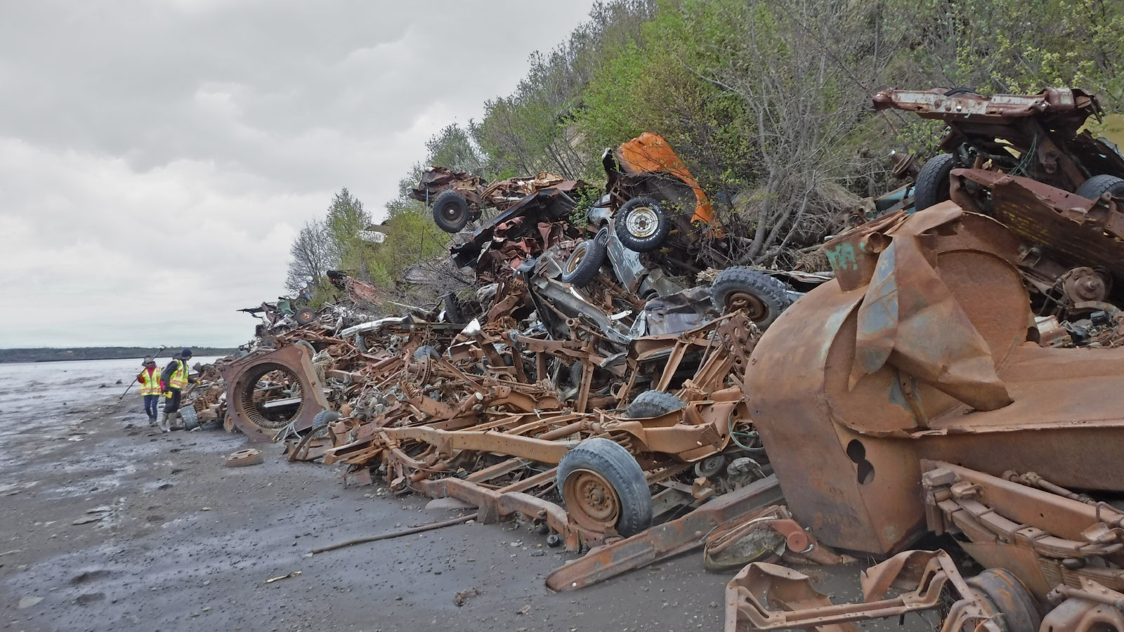 A pile of rusted cars and car parts are used as a barrier against an eroding coastline.
