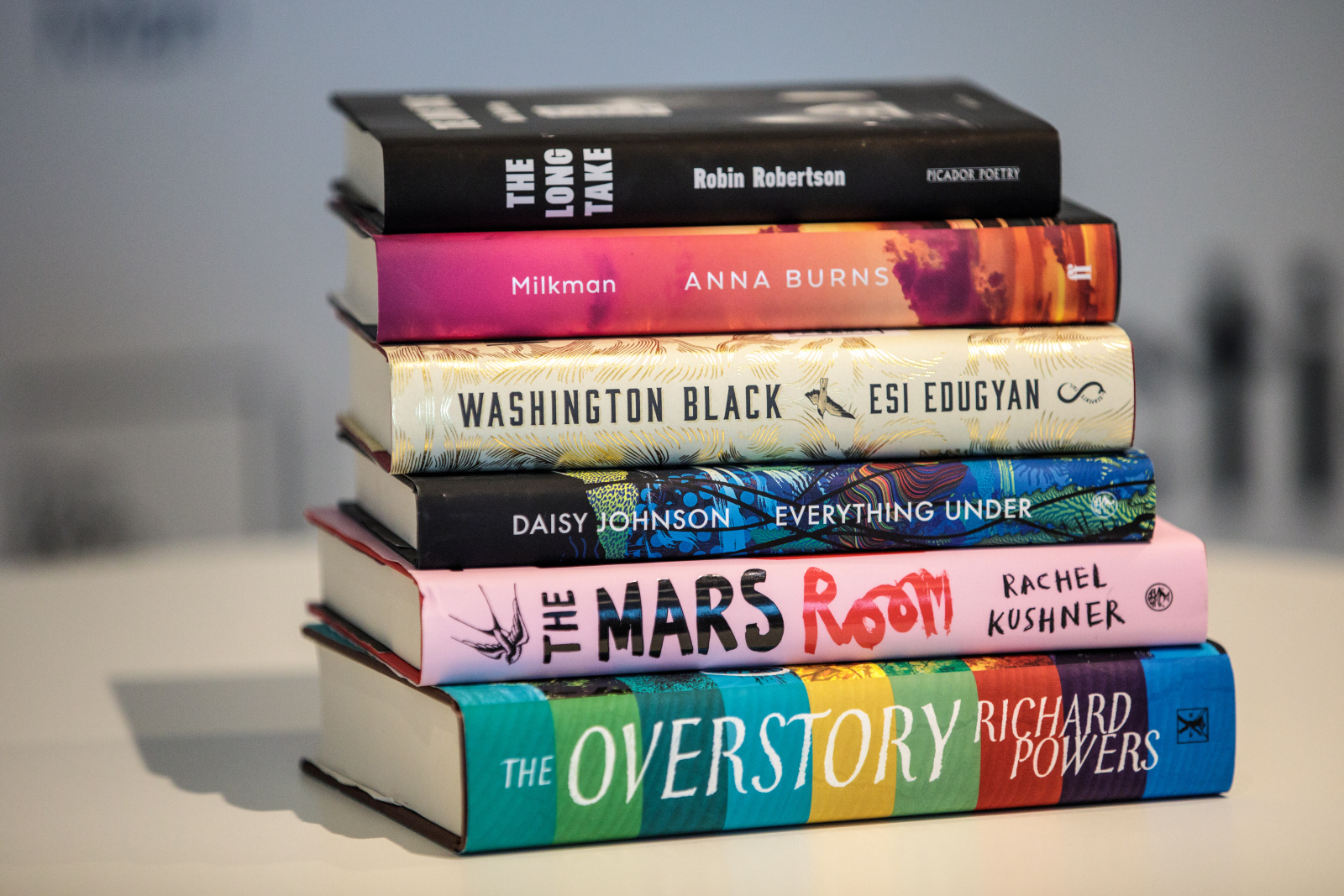 A stack of books includes The Long Take, Milkman, Washington Black, Everything Under, The Mars Room, and The Overstory.