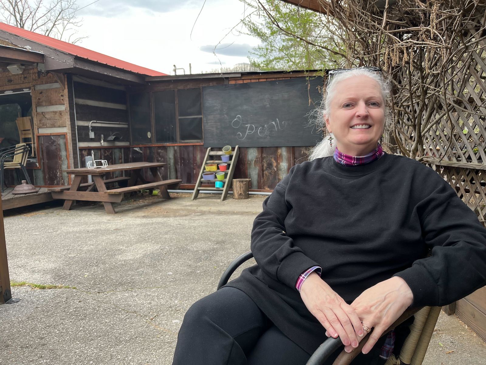 Jamie Brown, an environmental justice organizer from Hartford, Tennessee, sits in a deck chair outside a cafe. She wears a black shirt over a red plaid turtleneck and black pants.