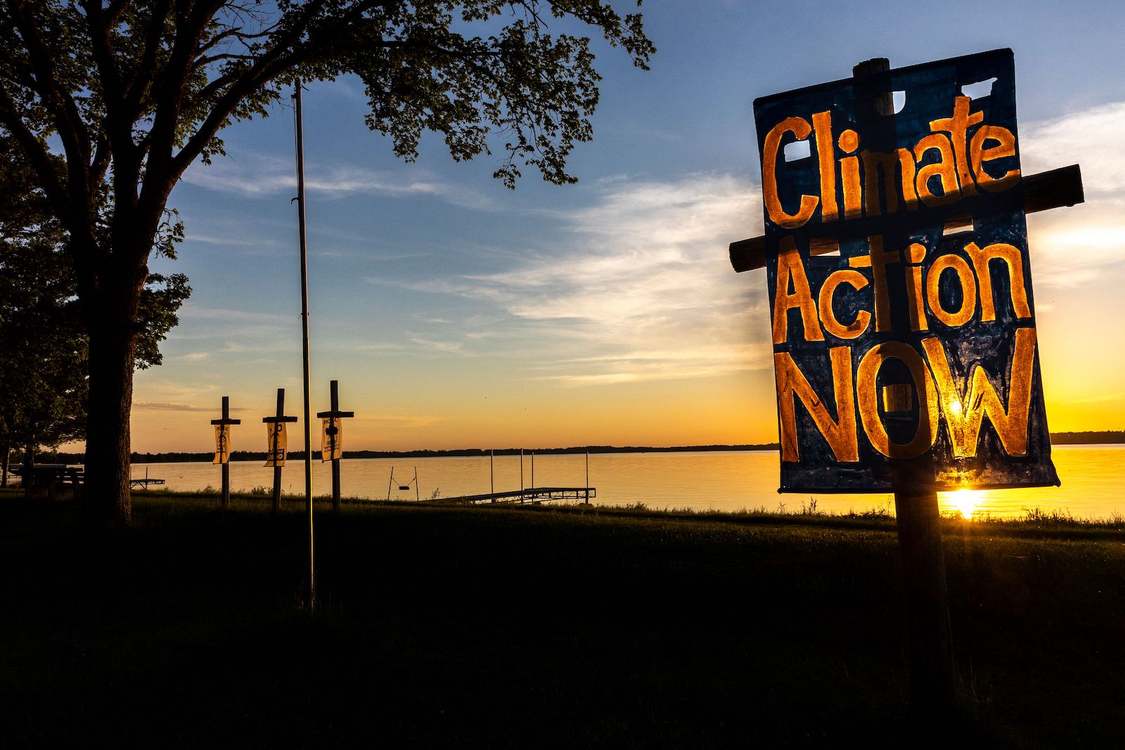 a cross with a banner that says climate action now at sunset