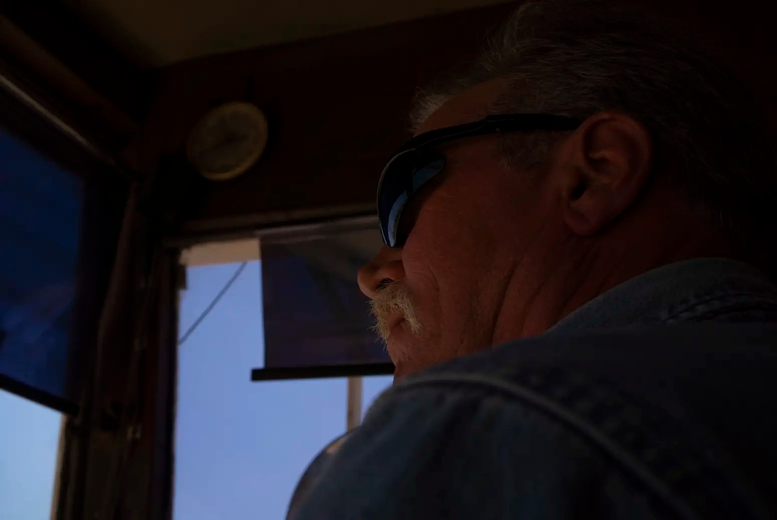 A portrait of an older man in sunglasses sitting in a truck.