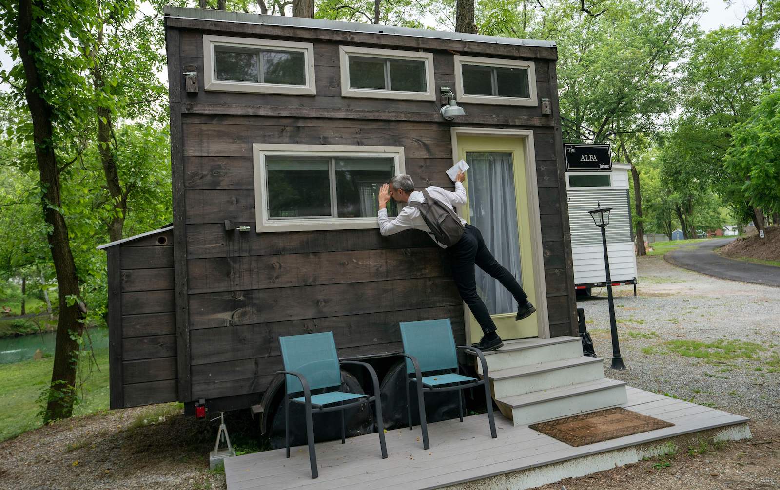 A man with a camera peers through the windows of a tiny house
