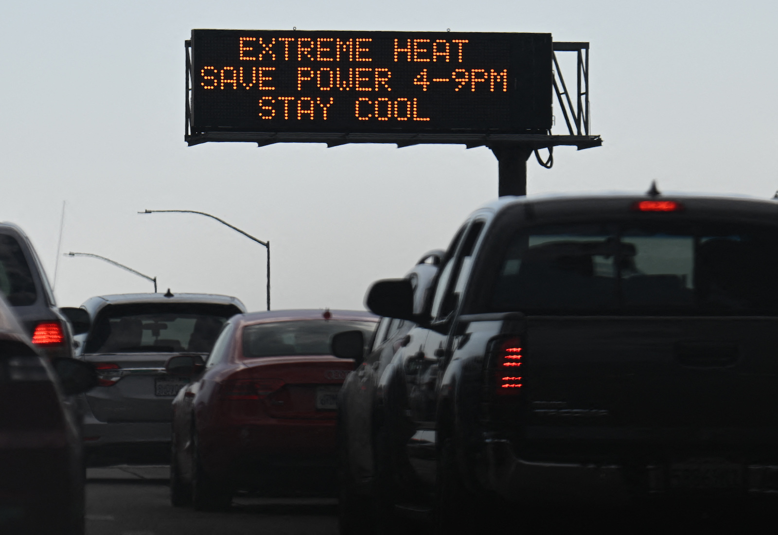 Cars drive past sign reading "Extreme heat, save power 4-9pm, stay cool."