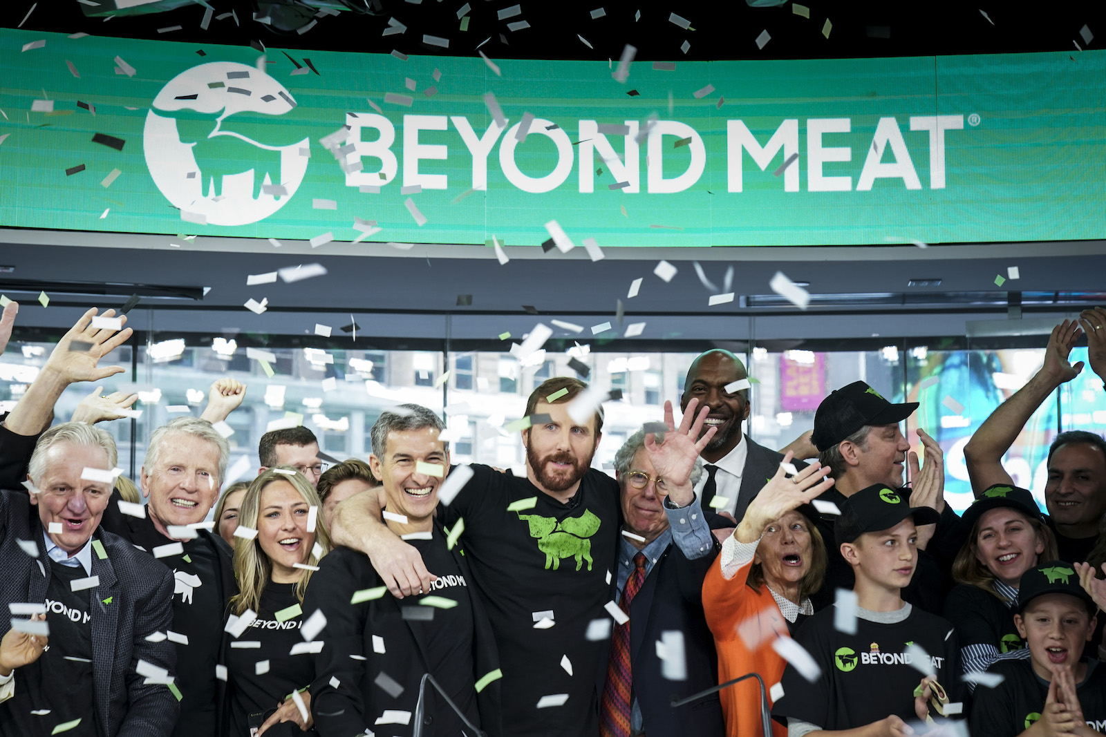 a bunch of people celebrate in front of a beyond meat sign in the stock market with ticker tape falling