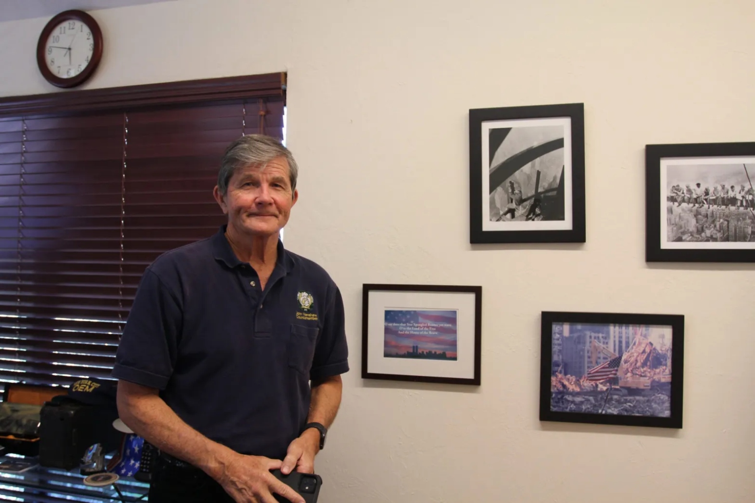 John Henshaw stands next to a photo gallery of 9/11 photos on the wall.