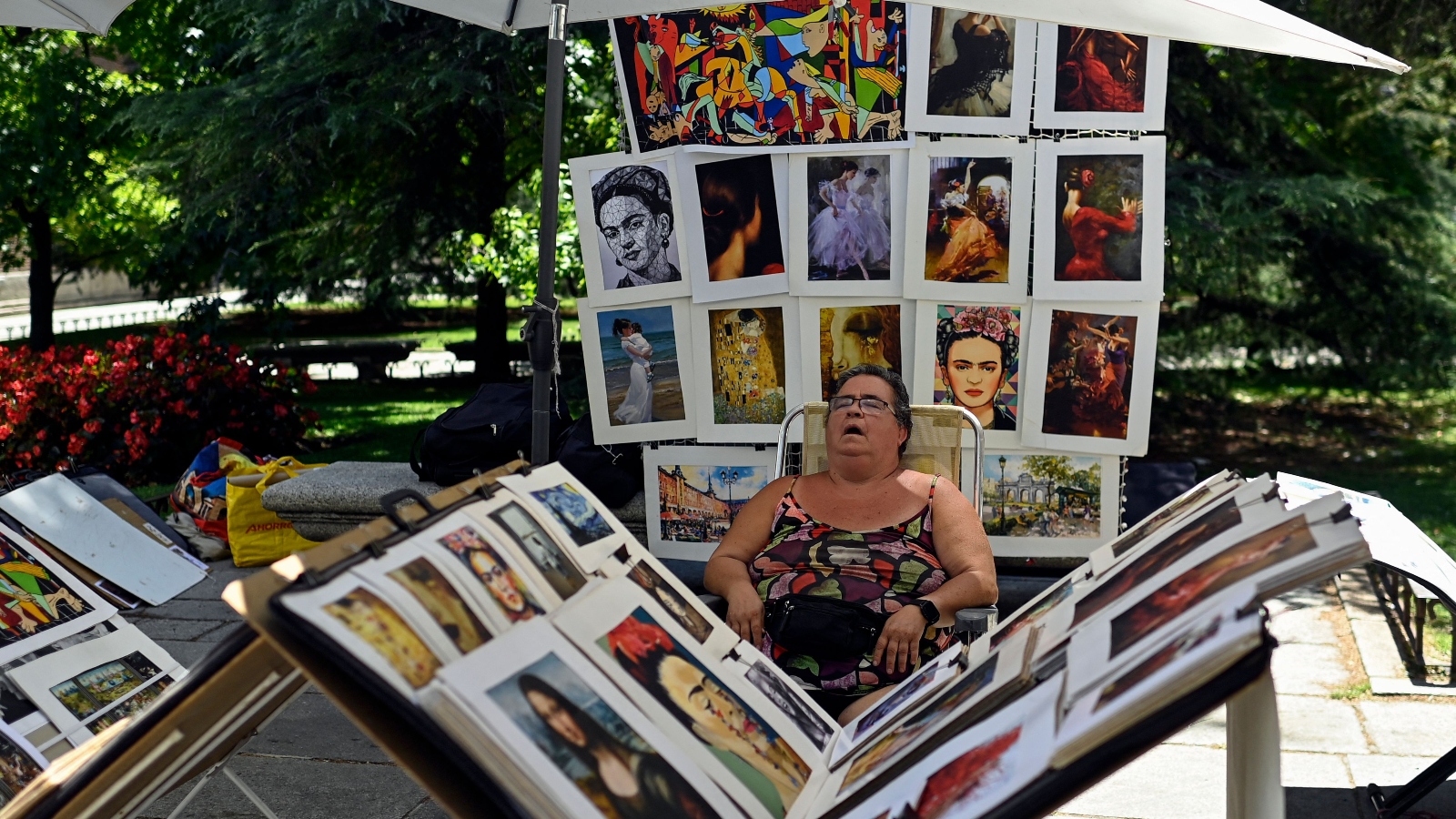 An art seller naps near her outside stand, filled with prints from artists like Frida Kahlo, Gustav Klimt, and Pablo Picasso