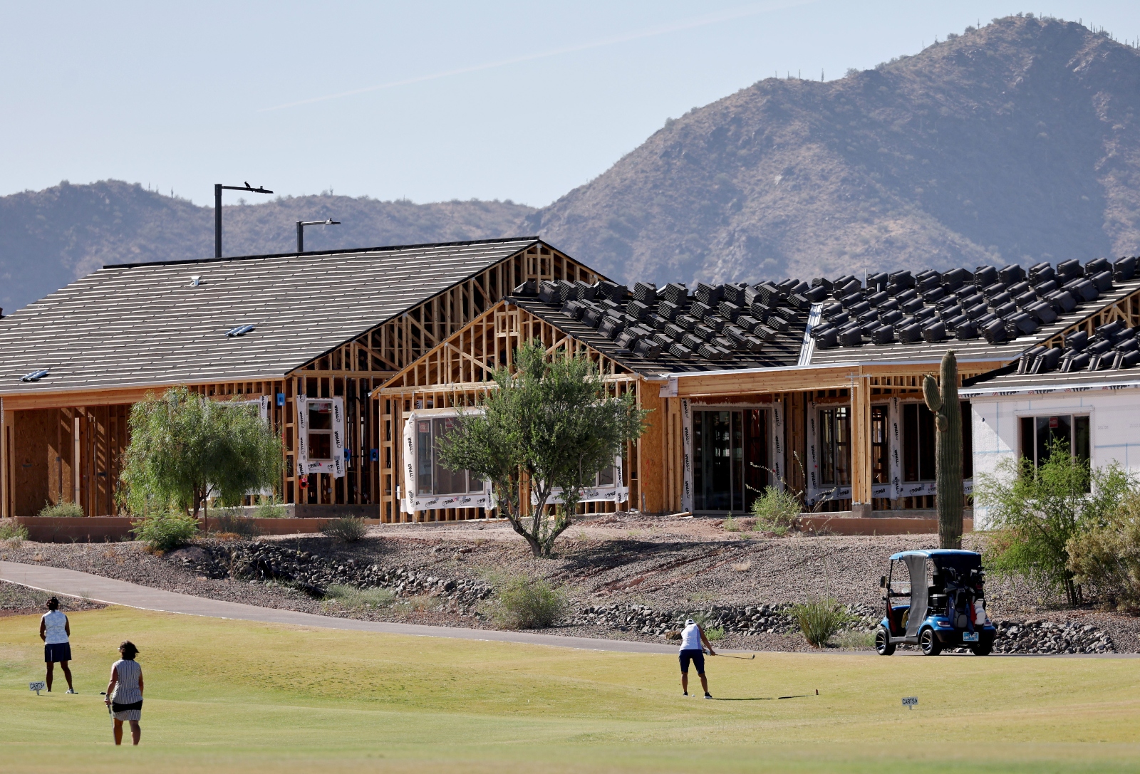 A man golfs in front of a house under construction in front of a mountain.