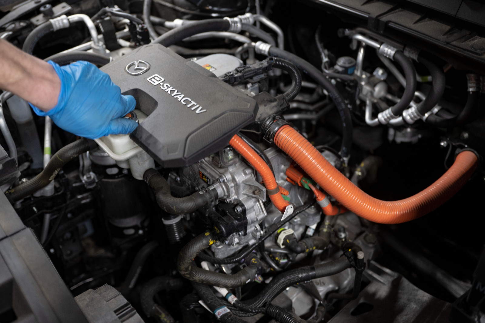 A hand wearing a blue disposable glove touches the inner workings of an electric car