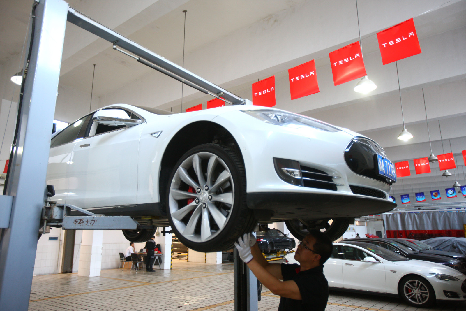 A man stands underneath a white Tesla car in a repair shop