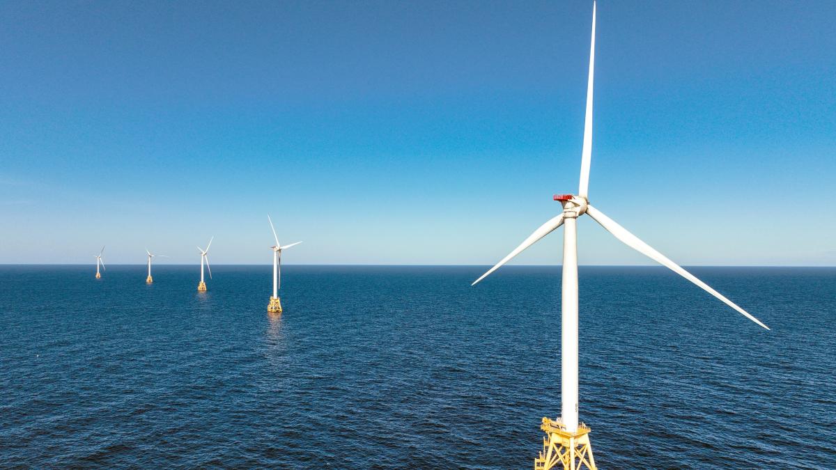 A line of wind turbines in the ocean under a blue sky.
