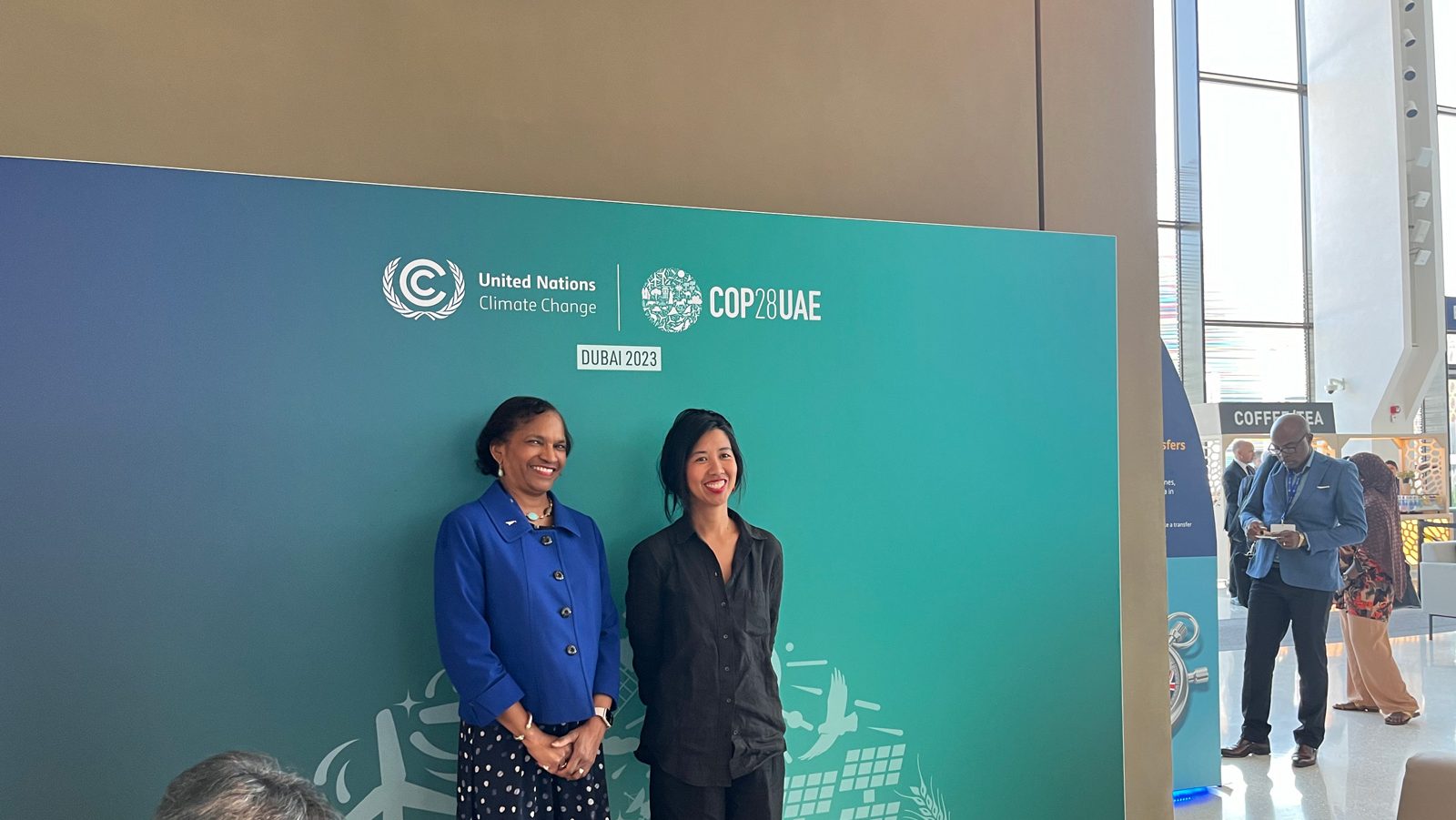 Two women stand before a COP28 sign for a photo