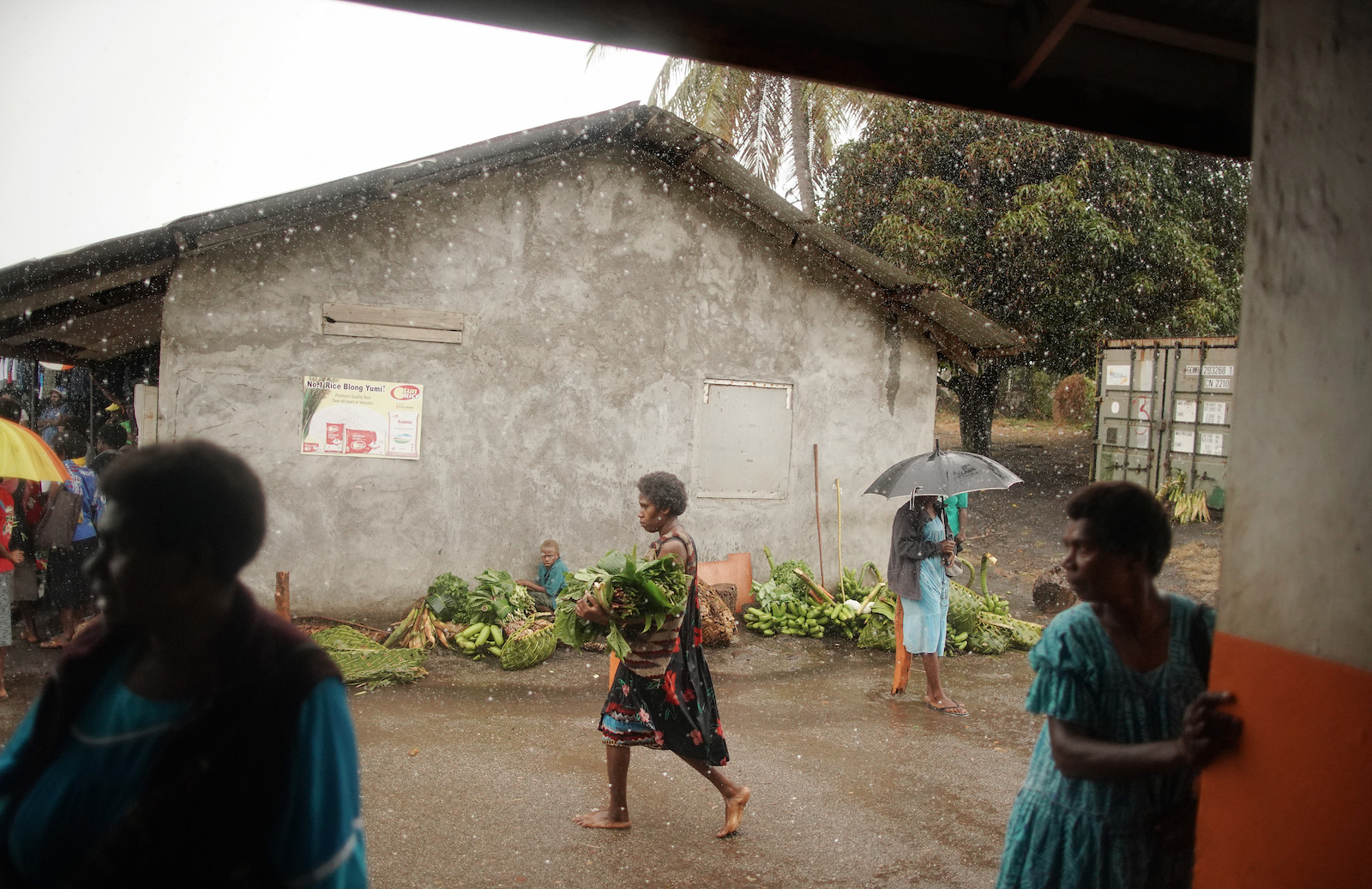 a woman walks by while people gather under an awning in the rain
