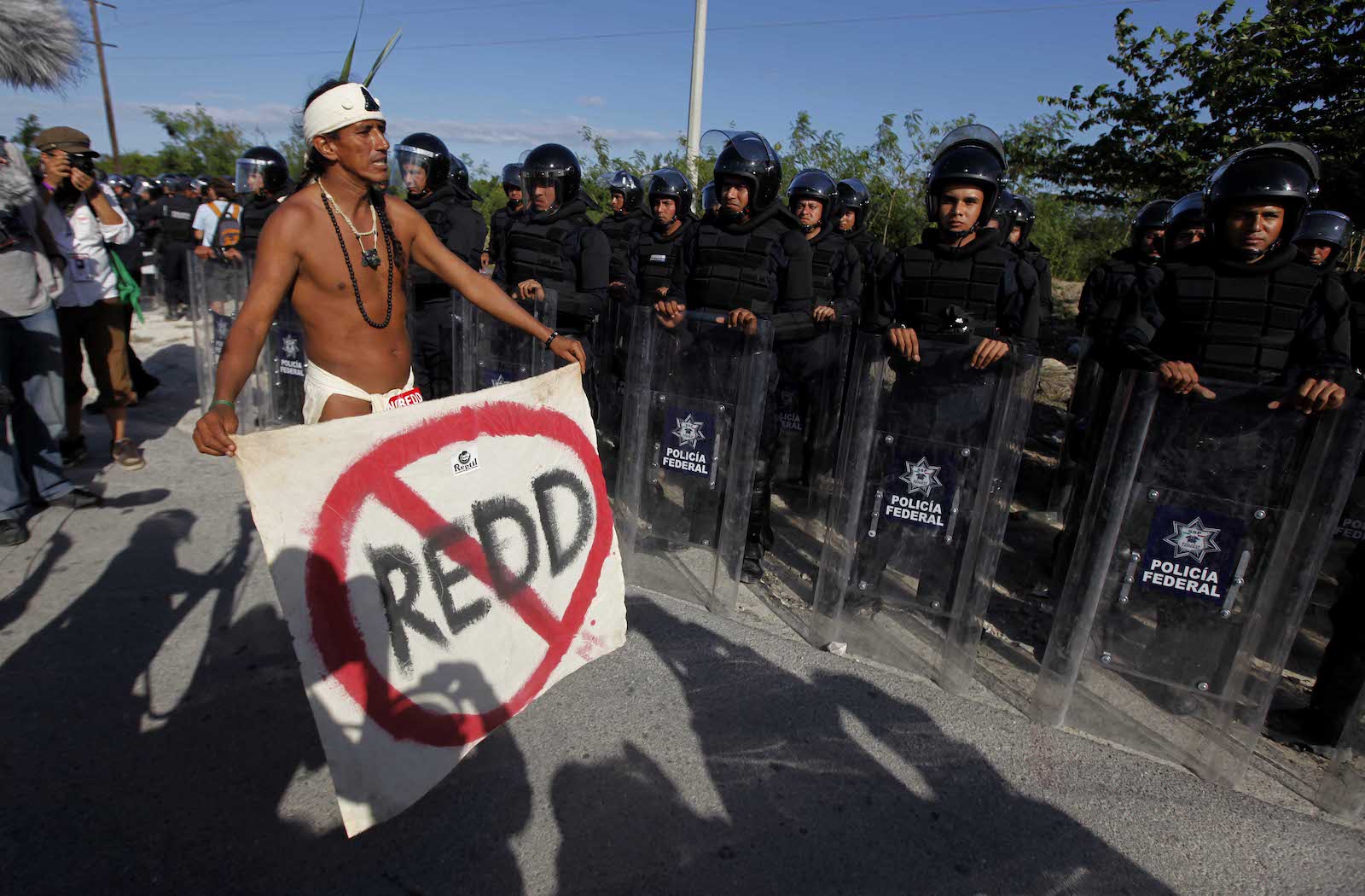 a man holds a sign that says REDD with a slash through it while standing in front of police officers