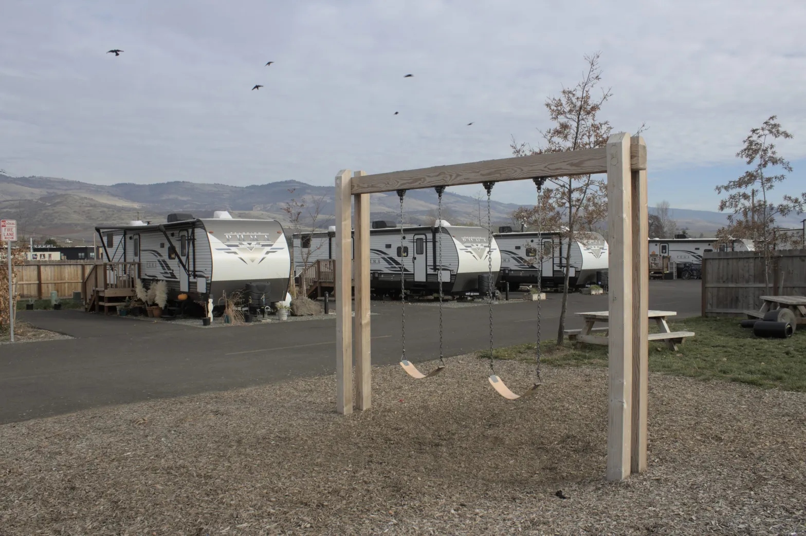An empty swing sets sits in front of a group of trailers.