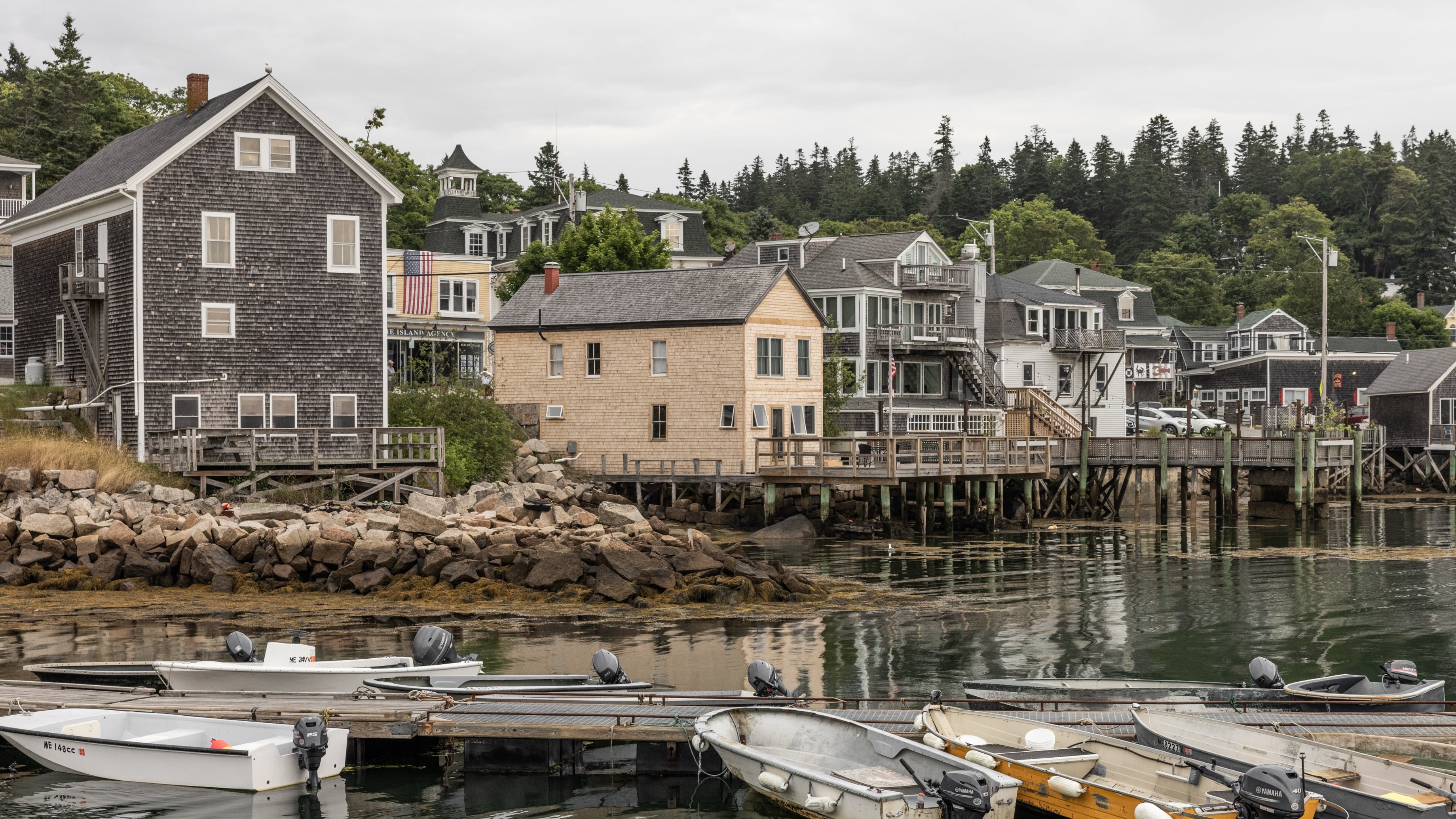A quaint Maine town with shingled homes sitting on the water next to small boats.